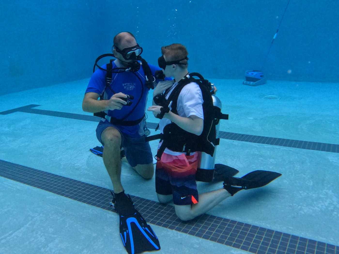 An instructor kneeling face to face with a student on the bottom of the pool, guiding a scuba skill